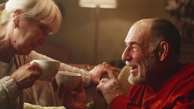 Elderly Couple with Tea Speaking in Living Room.