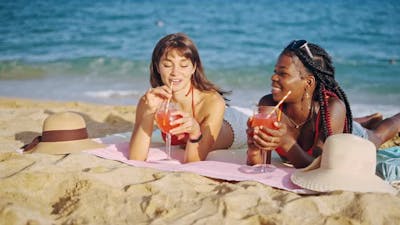 Two Girls Lying on Beach with Fruit Cocktails.