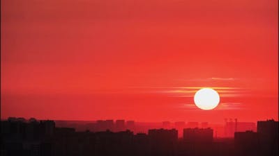 The big red sun sets behind the roofs of houses at sunset, timelapse.