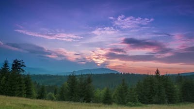 Sunset in the Cloudless Sky over Wooded Mountains.