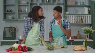 Millennial African American Couple in Aprons Cooking Fresh Salad Together in Kitchen and Drinking.