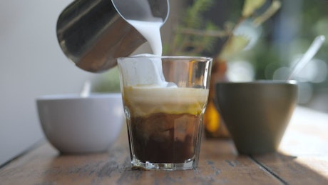 A barista preparing coffee with milk and ice.