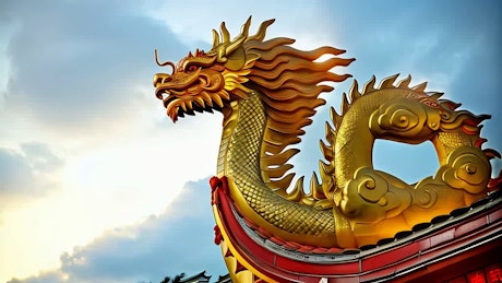 A mighty golden dragon statue under a blue sky with fireworks exploding on the Chinese New Year celebration.