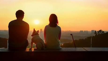 A young couple sitting at the park with a dog share a heartfelt kiss at dusk.