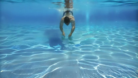 A young man swims on a crystal clear pool on a sunny day.