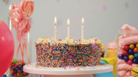 Birthday cake on a table with candies and balloons.