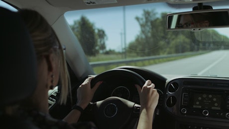 Blonde woman driving on road.
