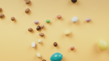 Chocolate eggs rolling on a yellow background.