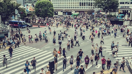 Crowds of people cross a street junction.