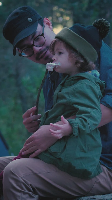 Father and his little daughter eating marshmallows in nature.