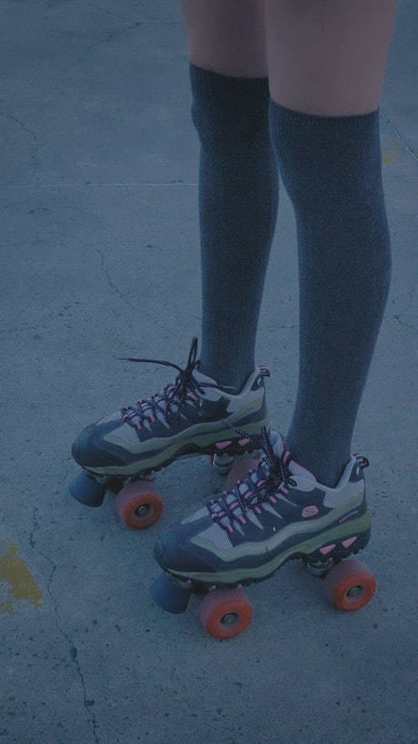 Girl with roller skates standing in the middle of a parking lot.