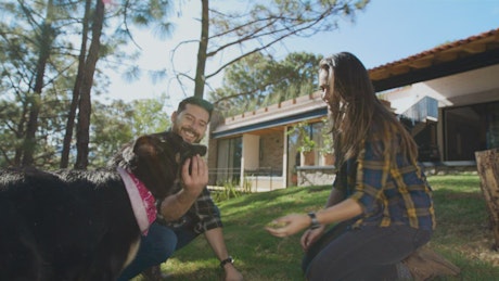 Man and woman playing with a dog in a garden.