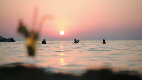 People playing ball in the ocean at sunset.