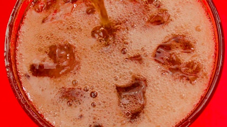 Pouring coke on a glass with ice generates soda bubbles and foam.