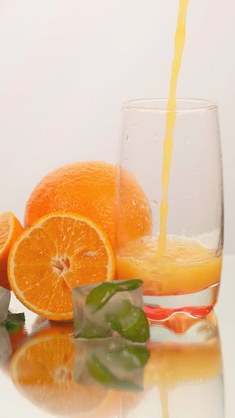 Serving juice in a glass with some oranges on a white background.