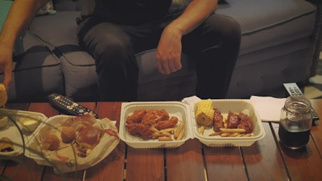 Table in a living room with fast food while a man watches television.