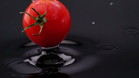 Tomato falling into black water.