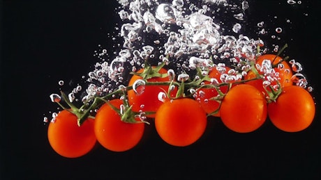 Tomatoes falling through water, black background.