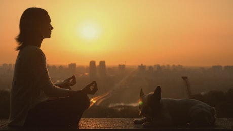 Woman meditating with her dog in the sunset.