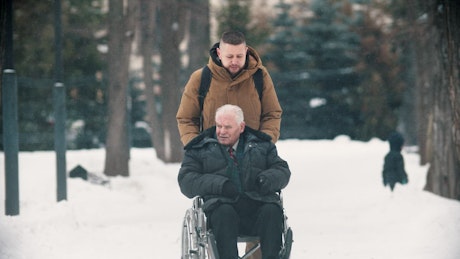 Young man walking with grandfather in a wheelchair.