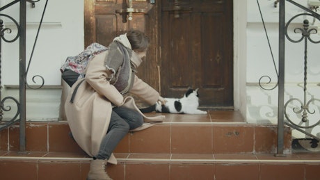 Young woman playing with a kitten on the steps of a house.