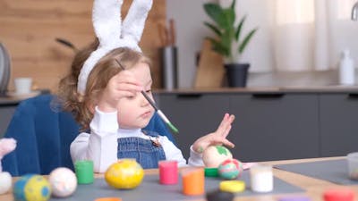 A Little Girl in Bunny Ears Painting Easter Eggs at a Table.