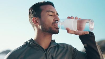 Beach, exercise and man drinking water, wellness and workout with hydration.