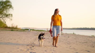 Young Woman Enjoying Evening Walk with Her Pet Dog on the Beach in Summer.