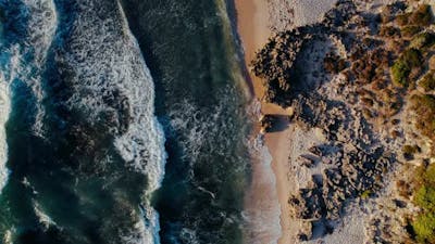 Aerial View of Waves Crashing on a Rocky Shoreline at Sunset.