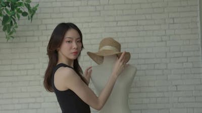 female fashion designer places a meticulously hat on a mannequin.
